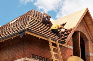 Homeowner inspecting roof shingles and clearing leaves from a gutter before a severe storm